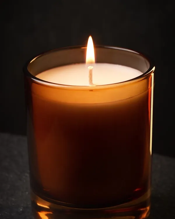 Free photo example: a lit candle in an amber glass jar on dark stone